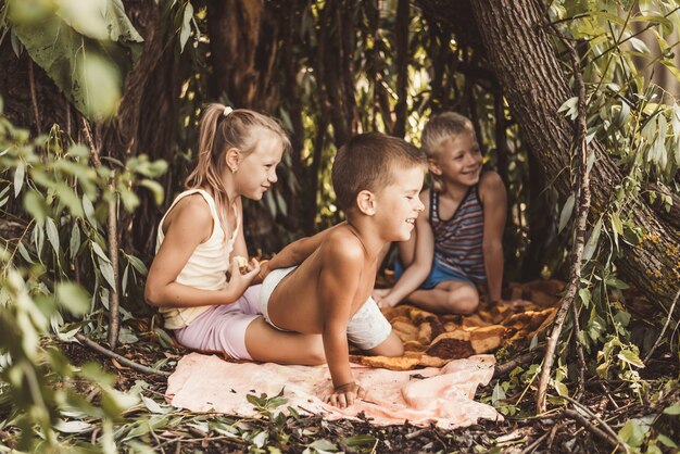 Três crianças da aldeia estão brincando em uma cabana que elas mesmas construíram com folhas e gravetos