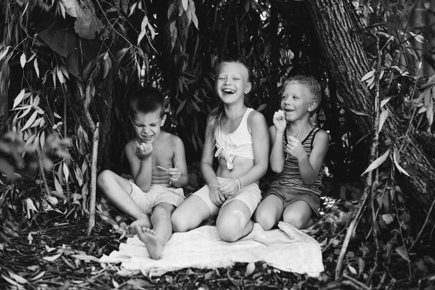 Três crianças da aldeia estão brincando em uma cabana que eles mesmos construíram com folhas e galhos Casa de madeira na floresta Fotografia em preto e branco