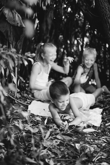 Três crianças da aldeia estão brincando em uma cabana que eles mesmos construíram com folhas e galhos Casa de madeira na floresta Fotografia em preto e branco
