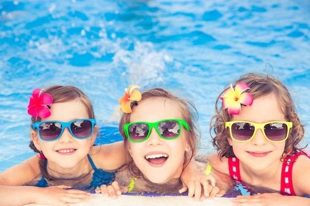 Três crianças felizes com óculos de sol coloridos na piscina