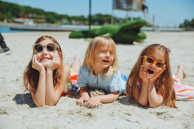 Três crianças felizes deitam na areia na praia uma criança com síndrome de down com amigos se diverte na praia