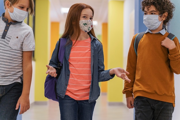 Foto três crianças no corredor da escola com máscaras médicas