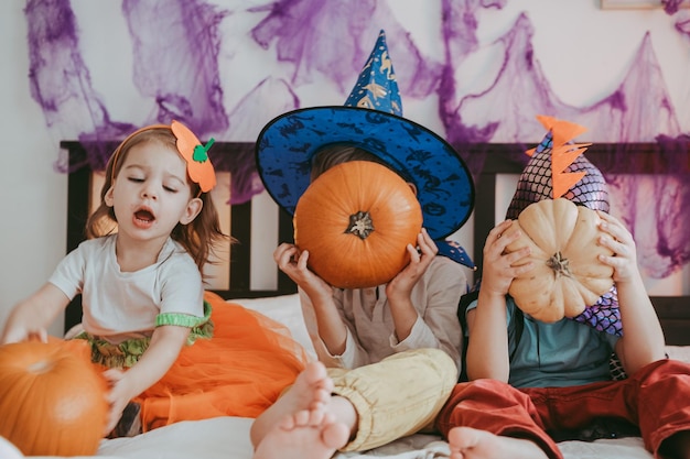 Três crianças pequenas em trajes festivos de Halloween com abóboras se divertindo passando tempo em família