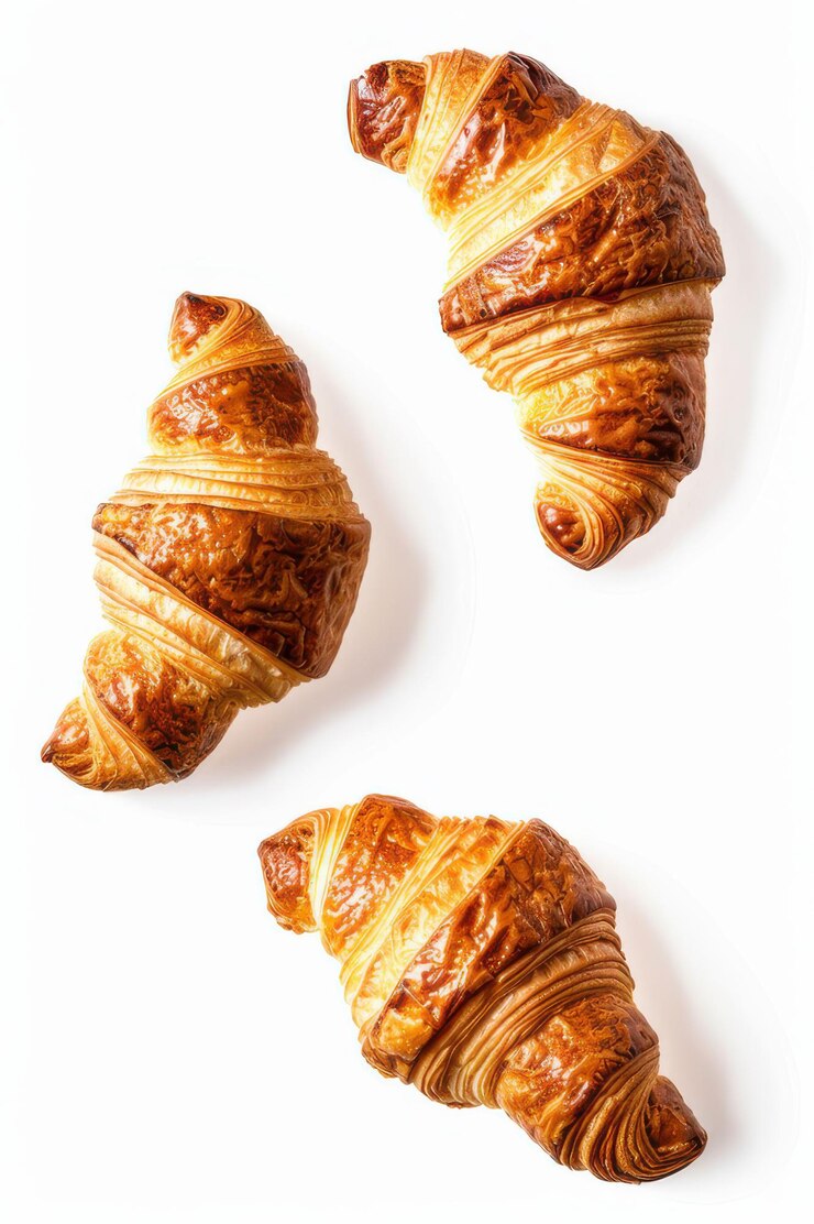 Tres croissants perfectamente horneados con capas de escamas doradas flotando sobre un fondo blanco ideales para conceptos de desayuno