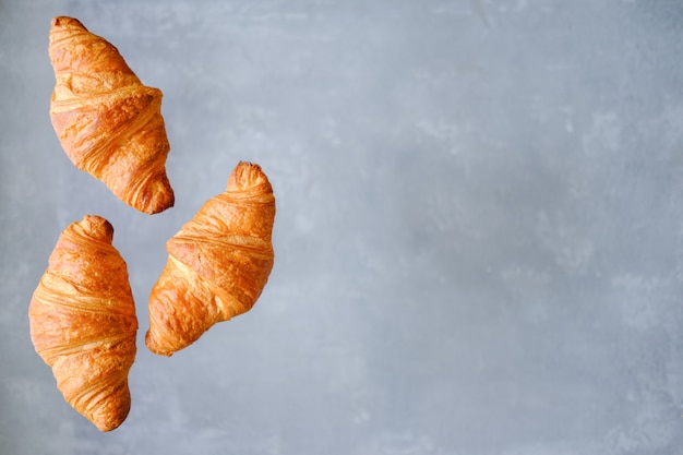 Três croissants recentemente cozidos que voam no fundo cinzento. Lugar para texto. Conceito de padaria criativa.