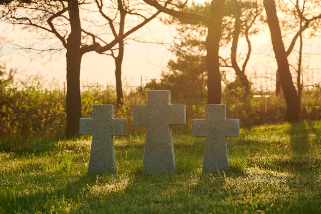 Tres cruces de piedra católica sobre la hierba verde al atardecer en el cementerio militar alemán en Europa. Monumento a los soldados muertos de la Segunda Guerra Mundial en Baltiysk, óblast de Kaliningrado, Rusia