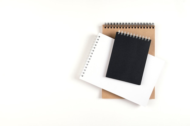 Tres cuadernos en blanco en una espiral apilados en una pila sobre un fondo blanco. Cuadernos con hojas blancas, negras y recicladas. Educación, oficina.