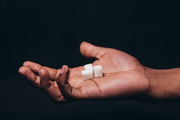 Três cubos de açúcar branco na palma da mão do homem negro, cena escura, close-up