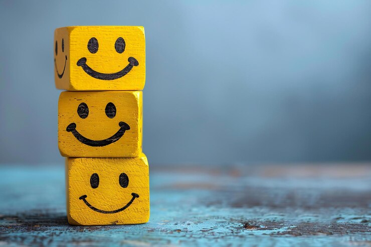 Tres cubos de madera amarillos apilados uno encima del otro con iconos de caras sonrientes felices colocados en ellos