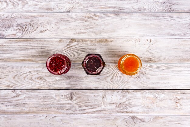 Tres cuencos con diferentes mermeladas en mesa de madera. Vista superior.