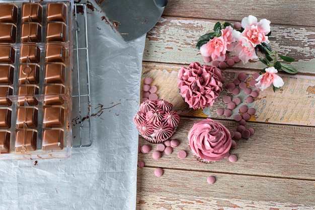 Tres cupcakes de chocolate con crema de mantequilla rosa. Junto a callets de chocolate Ruby, forma de policarbonato y espátula de acero inoxidable.