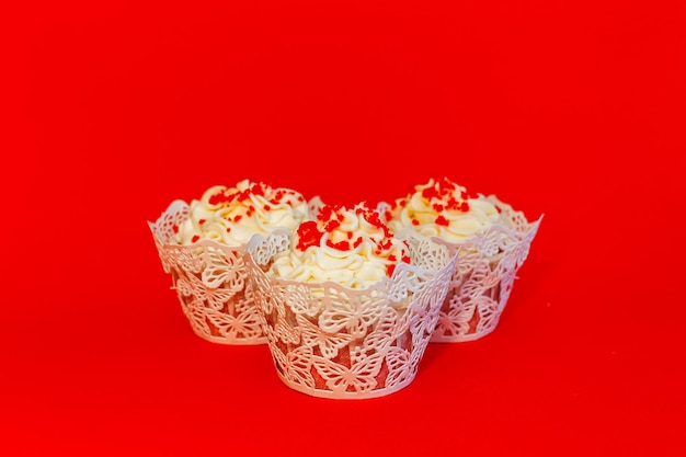 Tres cupcakes con delicada crema blanca sobre un fondo rojo.