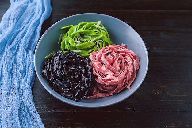 Tres deliciosas pastas. pasta negra, pasta verde y pasta fucsia. placa gris sobre una mesa de madera.