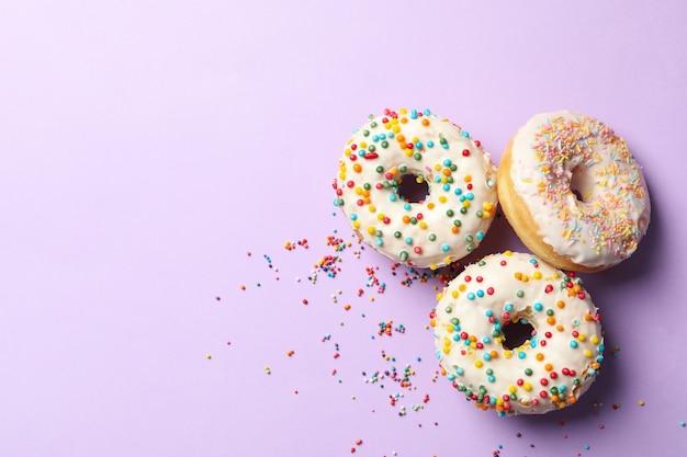 Três deliciosos donuts em fundo violeta, vista de cima