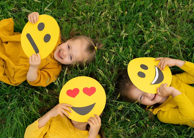 Tres divertidas chicas felices se esconden y miran detrás de las caras de los emoticonos