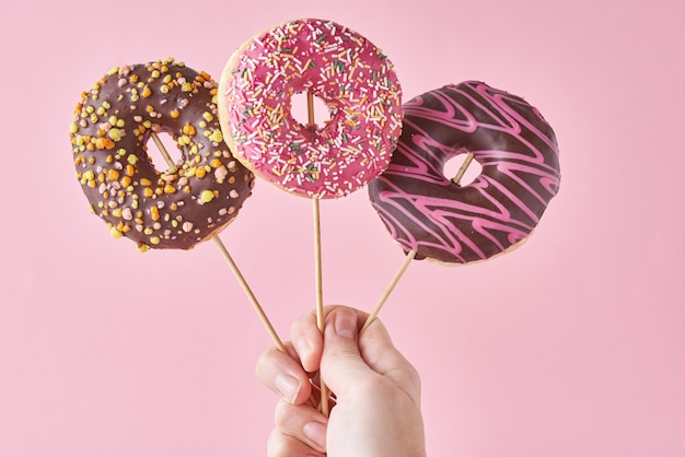 Tres donas en mano de mujer en superficie rosa. Comida creativa estilo minimalista