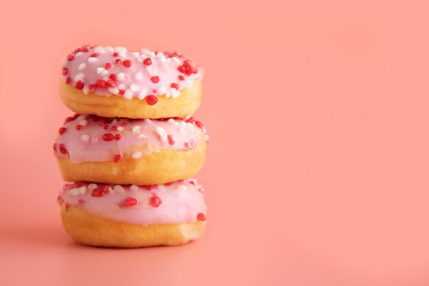 Três donuts com glacê rosa e decoração de framboesa mentem um sobre o outro no rosa