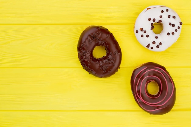 Tres donuts diferentes sobre fondo amarillo. Borde lateral de rosquillas variadas con glaseado de colores y chispas.