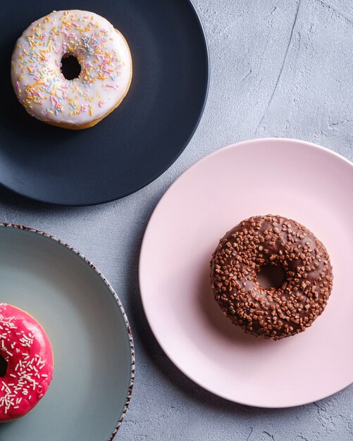 Três donuts em placas, chocolate, rosa e baunilha donut com granulado