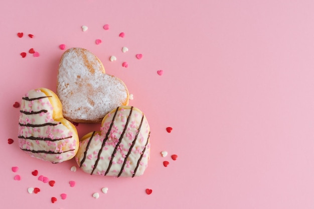 Tres donuts en forma de corazón sobre fondo rosa con decoración de topping de corazón Espacio de copia