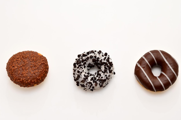 Tres donuts con glaseado y chocolate aislado sobre fondo blanco.