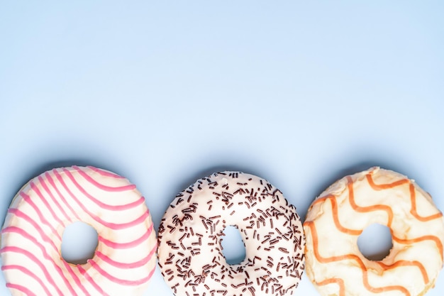 Foto três donuts multicoloridos em uma vista superior de fundo azul