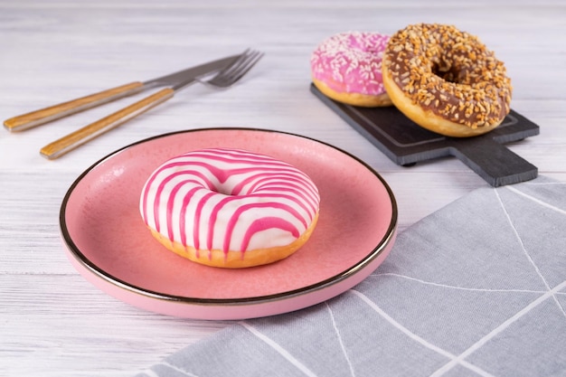 Três donuts revestidos de açúcar estão sobre uma placa de cerâmica rosa e uma tábua de corte de madeira Foco seletivo