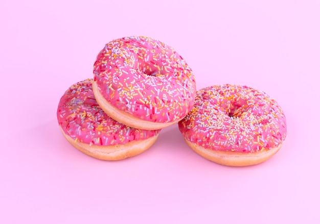 Três donuts rosa com pequenos doces em uma mesa rosa