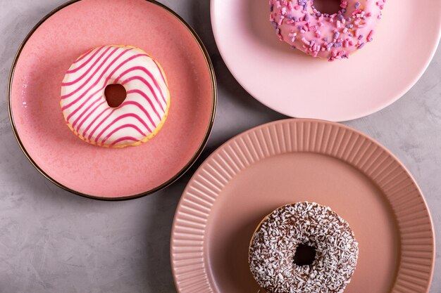 Três donuts vidrados deitam-se em altas placas cor-de-rosa em uma superfície cinzenta Foco seletivo Vista de cima