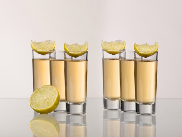 Três doses de tequila dourada com limão no fundo branco