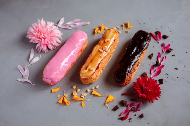 Três eclairs coloridos entre flores e decorações. sobremesa saborosa e deliciosa.