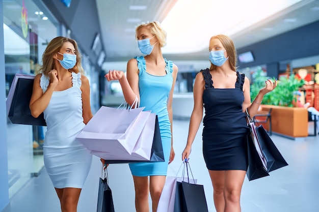 Foto tres elegantes mujeres sosteniendo bolsas de la compra después de la venta de compras el viernes negro de consumismo