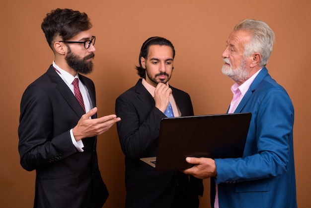 Tres empresarios barbudos multiétnicos juntos contra la pared marrón