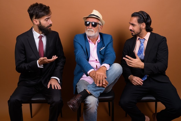 Três empresários barbudos multiétnicos juntos contra uma parede marrom