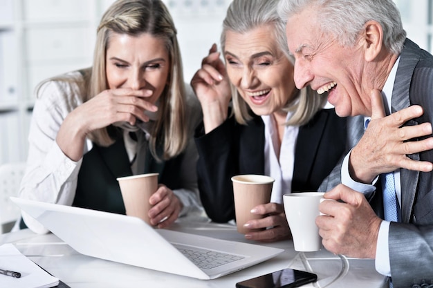 Três empresários maduros usando laptop enquanto estão sentados à mesa