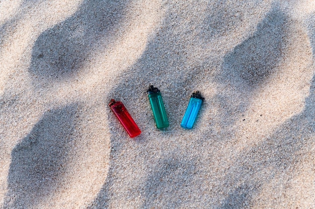 Tres encendedores rojo verde y azul tirados en la arena contaminando la playa y los mares