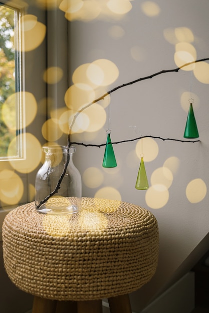 Foto três enfeites de natal de vidro verde em um galho de madeira em um vaso em um fundo de luz amarela bokeh turva. ideia criativa de decoração de quarto de ano novo e natal diy. ornamento escandinavo mínimo.