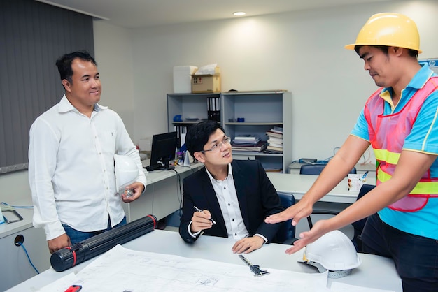 Três engenheiros asiáticos que procuram o plano de papel do edifícioDiscutem sobre os problemas e soluções de