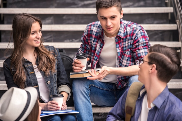 Três estudantes novos que aprendem em escadas na faculdade.