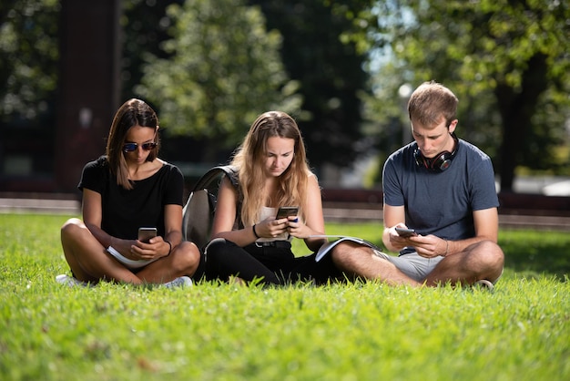 Três estudantes universitários sentados juntos conversando em seus telefones celulares