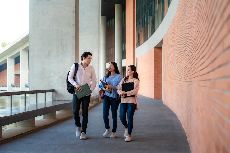 Foto tres estudiantes asiáticos están caminando y hablando juntos en la sala de la universidad durante las vacaciones en la universidad.
