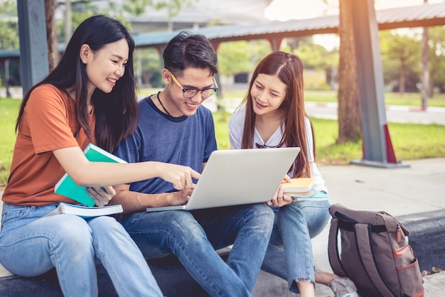 Tres estudiantes asiáticos jóvenes del campus disfrutan de la tutoría y la lectura de libros juntos