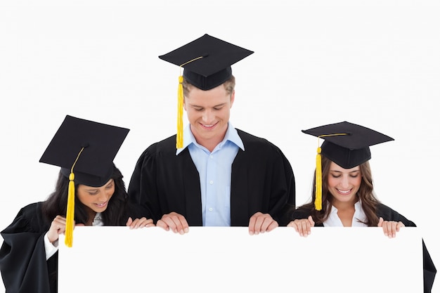 Tres estudiantes que se han graduado sosteniendo la hoja en blanco y mirándolo