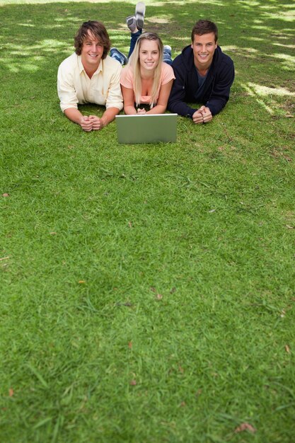 Tres estudiantes sonrientes tendidos en un parque