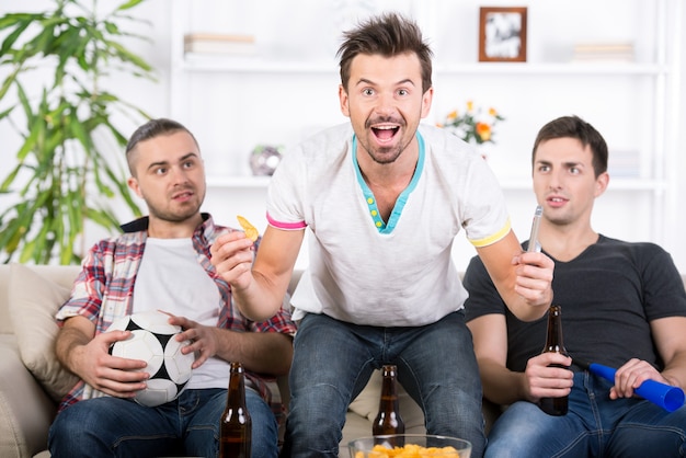 Três fãs de futebol estão torcendo jogo de futebol em casa.