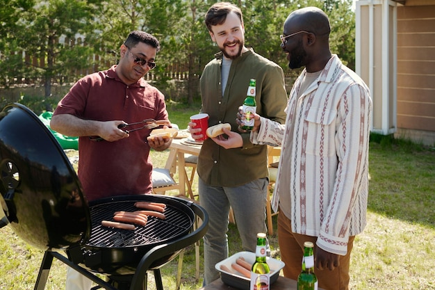 Tres felices jóvenes interculturales tomando cerveza y charlando al aire libre