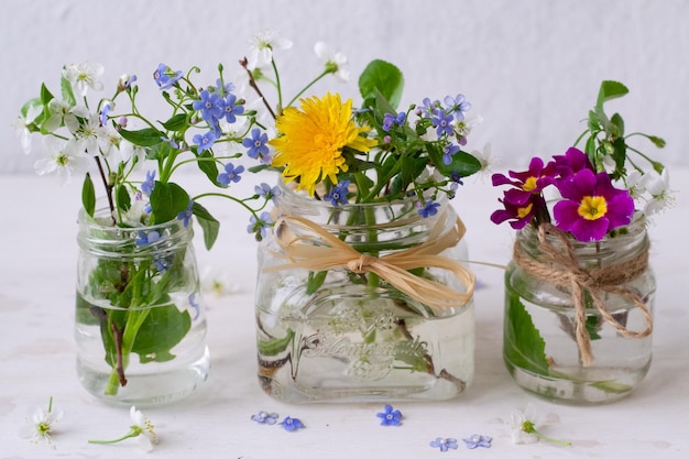 Tres frascos de vidrio con flores con una cinta atada alrededor de ellos, uno de los cuales dice 'dientes de león'