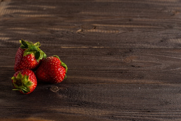 Tres fresas frescas y jugosas se encuentran en una mesa vieja de un fondo de madera oscura.