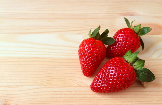 Tres frutas de fresa maduras frescas de color rojo vibrante aisladas en mesa de madera