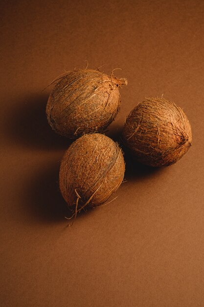 Tres frutos de coco sobre fondo liso marrón vibrante, concepto tropical, ángulo de visión